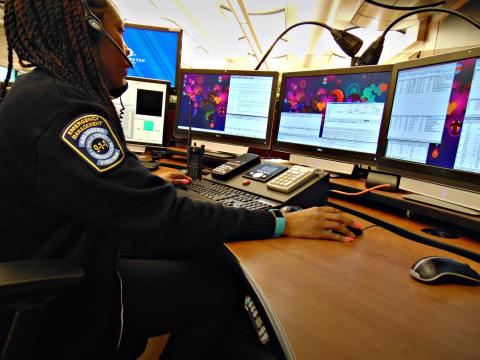 public safety telecommunicator sitting at a desk with four computer screens